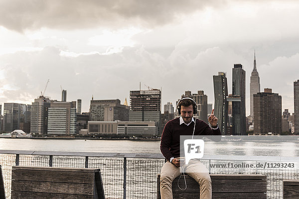 USA  New York City  junger Mann mit Kopfhörer und Handy am East River