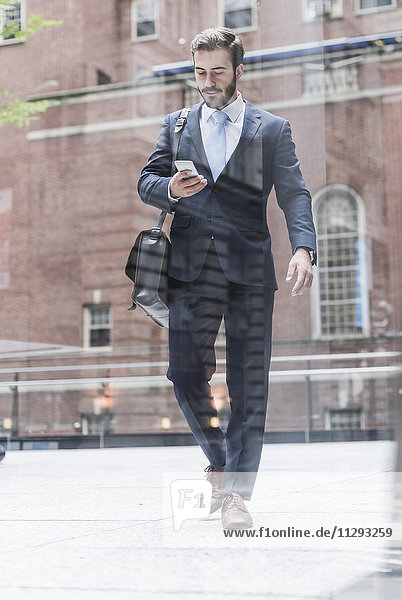 USA  New York City  businessman walking in Manhattan looking at cell phone