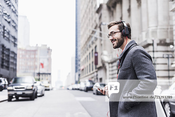 USA  New York City  lächelnder Geschäftsmann mit Handy und Kopfhörer unterwegs
