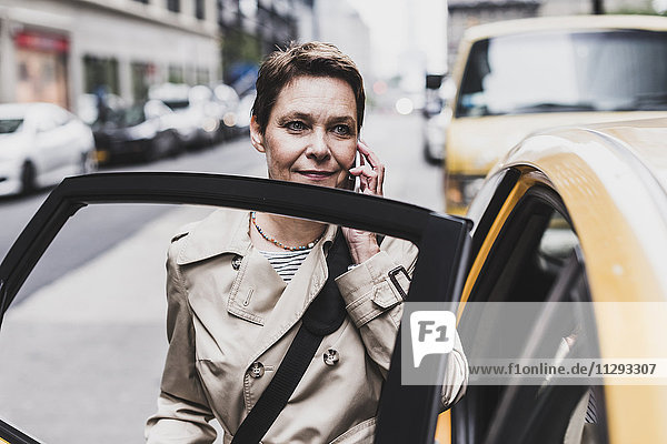 USA  New York City  Frau in Manhattan am Handy beim Einsteigen in ein Taxi