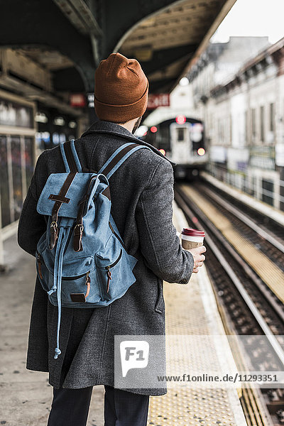 Junger Mann wartet am Bahnsteig der U-Bahn-Station  hält Einwegbecher