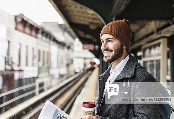 Young man waiting at metro station platform  holding disposable cup