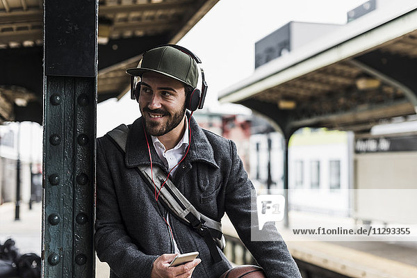 Young man waiting for metro at train station platform  wearing headphones