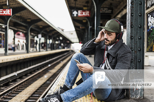 Junger Mann wartet auf die U-Bahn am Bahnsteig  mit Smartphone