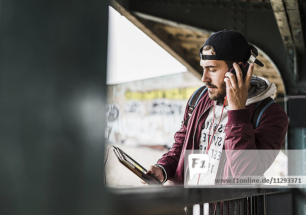 Junger Mann wartet auf U-Bahn  weraing Kopfhörer  mit digitalem Tablett