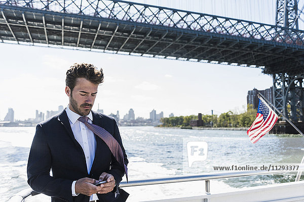 USA  New York City  Geschäftsmann auf der Fähre auf dem East River  der sein Handy überprüft.