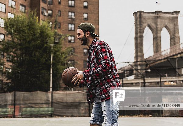 USA  New York  lachender junger Mann mit Basketball auf einem Außenplatz
