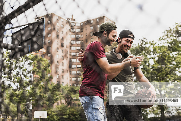 Two smiling friends with basketball and cell phone outdoors