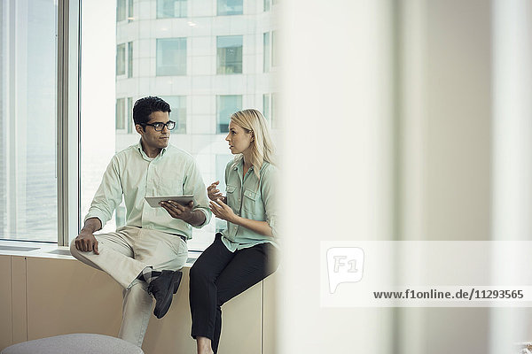 Business people with digital tablet sitting on window sill  discussing