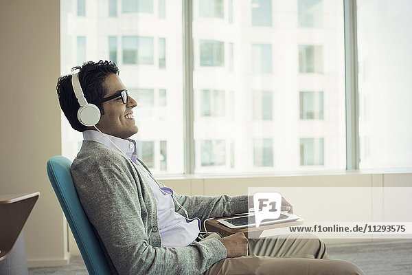 Businessman sitting in chair  wearing headphones  using digital tablet