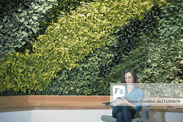 Geschäftsfrau mit Smartphone vor grüner Pflanzenwand
