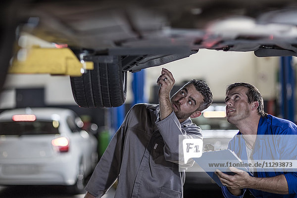Zwei Kfz-Mechaniker in einer Werkstatt  die das Auto gemeinsam untersuchen.