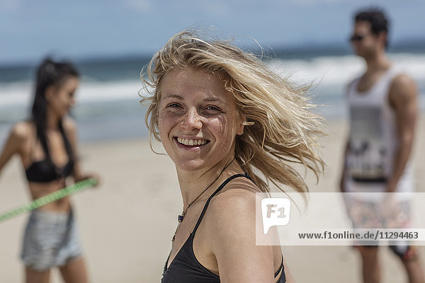 Fröhliche junge Frau am Strand mit Freunden im Hintergrund