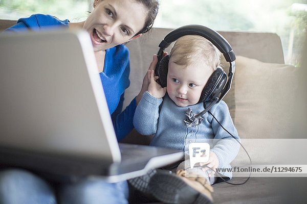 Mother with baby girl wearing headphones using laptop at home