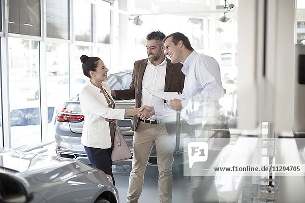 Car dealer shaking hands with woman in car dealership
