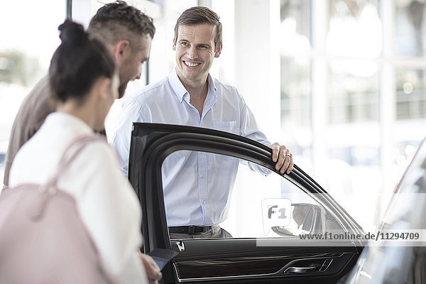 Car dealer showing car to couple in showroom