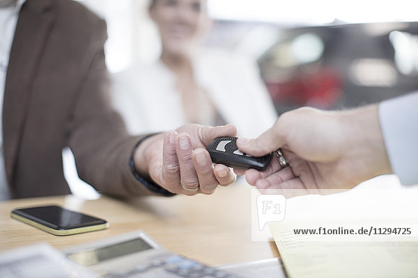 Car dealer handing over key to man at car dealership