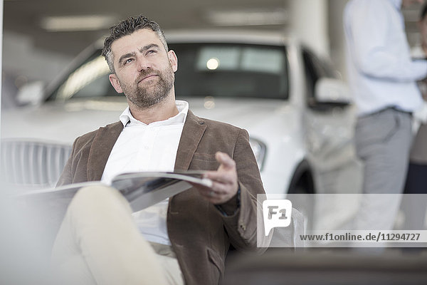 Man sitting with magazine at car dealership
