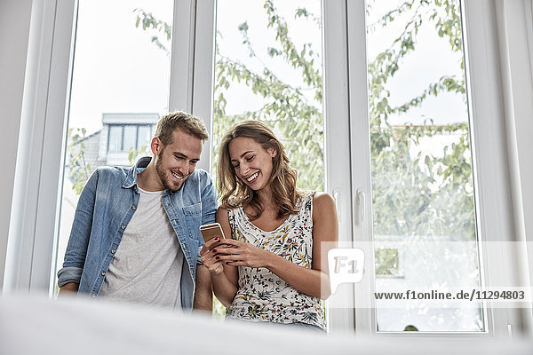 Lächelndes Paar vor dem Fenster mit Blick auf das Smartphone