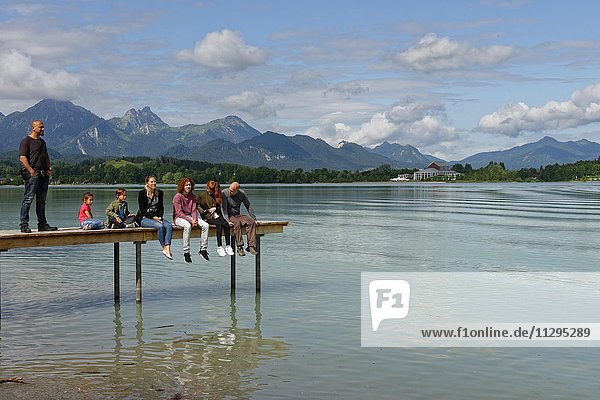 Family sitting on pier  Lake Forggensee  Füssen  Allgäu  Bavaria  Germany  Europe