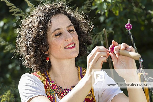 Button maker  young woman in colorful dirndl with Posamentenknopf Collier sitting in a garden  working on Posamentenknopf  Ichenhausen  Bavaria  Germany  Europe