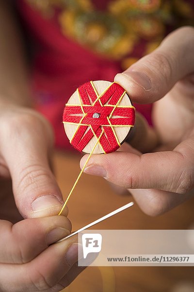 Knopfmacherin  Posamenten Knopf-Rohling aus Holz mit Haltewerkzeug  rotes Sternmuster wird zusätzlich mit gelbem Garn von Händen umwickelt und genäht  vierter Schritt