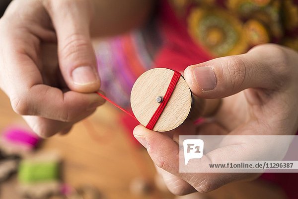 Knopfmacherin  Posamenten Knopf-Rohling aus Holz mit Haltewerkzeug wird mit rotem Garn von Händen umwickelt  erster Schritt