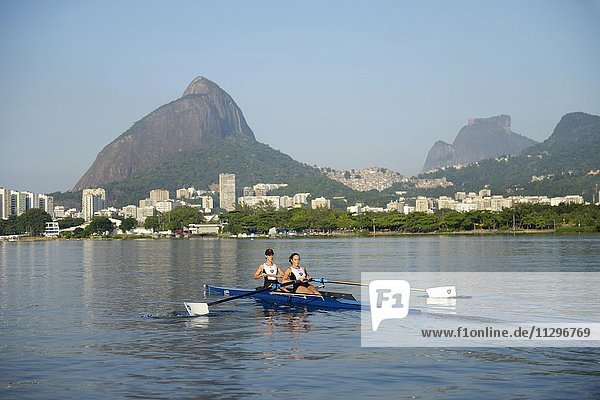Two young women participating in early morning rowing training in the Lagoa Rodrigo de Freitas Lagoon  with Rio de Janeiro skyline and Sugar Loaf Mountain  Lagoa District  Rio de Janeiro  Brazil  South America