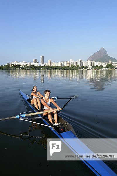 Two young women participating in early morning rowing training in the Lagoa Rodrigo de Freitas Lagoon  with Rio de Janeiro skyline and Sugar Loaf Mountain  Lagoa District  Rio de Janeiro  Brazil  South America