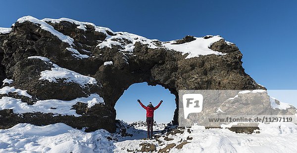 Frau steht vor Felsbogen  Lavafeld bedeckt mit Schnee  Vulkansystems Krafla  Dimmuborgir Nationalpark  Mývatn  Island  Europa