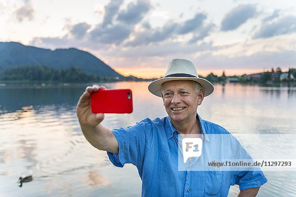 Mann lächelt  fotografiert sich mit einem Handy selbst  Selfie  Schliersee  Oberbayern  Bayern  Deutschland  Europa