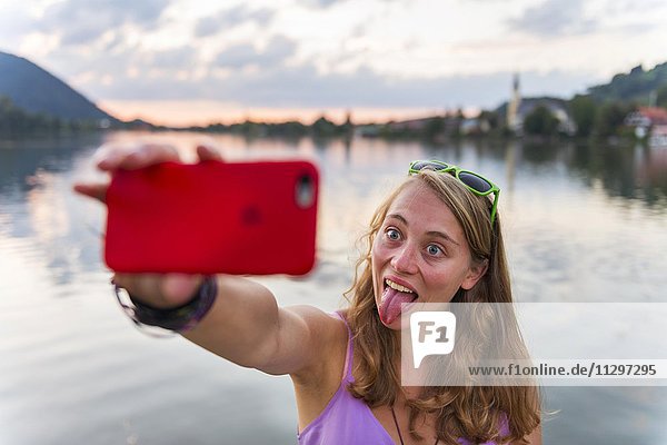 Junge Frau zieht Grimasse  fotografiert sich mit einem Handy  Selfie  Schliersee  Oberbayern  Bayern  Deutschland  Europa