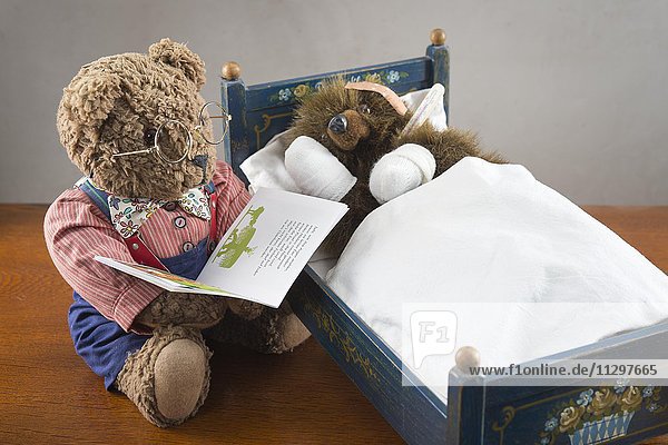 Kranker Teddybär  Pfoten verbunden  Pflaster auf Kopf  Fieberthermometer  liegt in Original Pumuckl Bettchen  grosser Bär mit Brille liest aus Buch vor