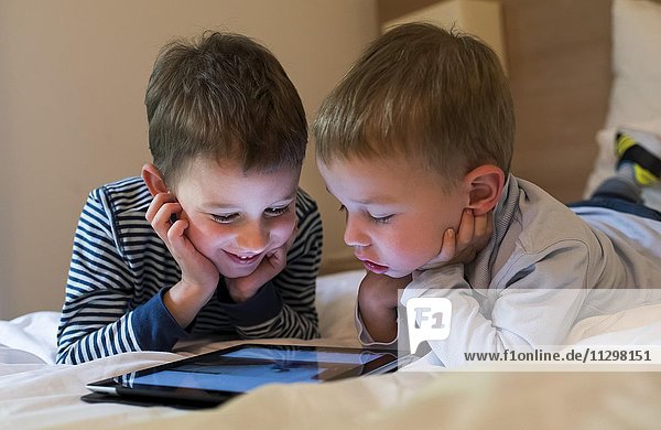 Two boys  siblings lying on a bed and playing with an iPad  Tablet PC