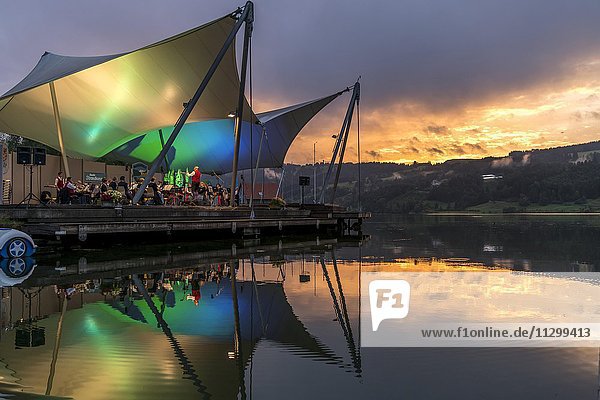 Strandkonzert bei Abenddämmerung mit der Musikkapelle Bühl auf der Seebühne  Großer Alpsee bei Bühl  Allgäu  Bayern  Deutschland  Europa