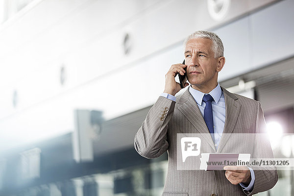 Businessman with passport and airplane ticket talking on cell phone in airport