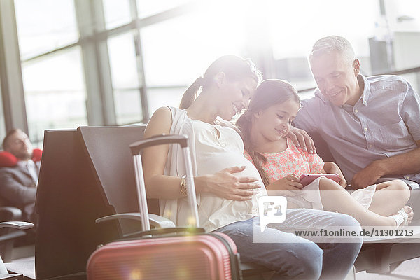 Schwangere Familie mit digitalem Tablett im Abflugbereich des Flughafens