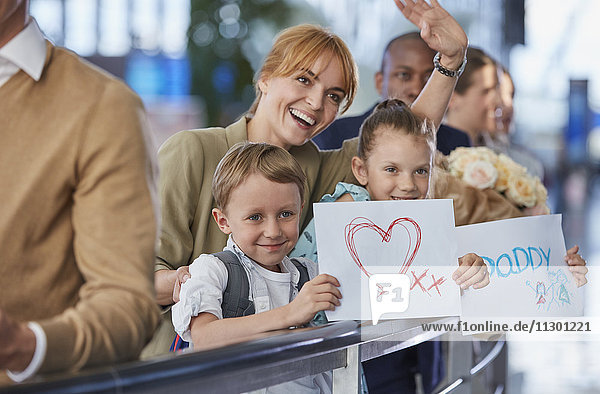 Mutter und Kinder mit Begrüßungsschildern für Vater am Flughafen