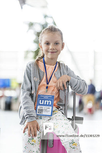 Portrait lächelndes Mädchen sitzend auf Koffer im Flughafen