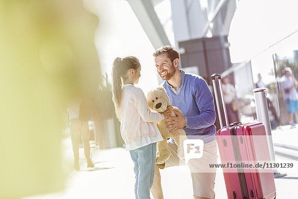 Vater und Tochter mit Teddybär und Koffer außerhalb des Flughafens