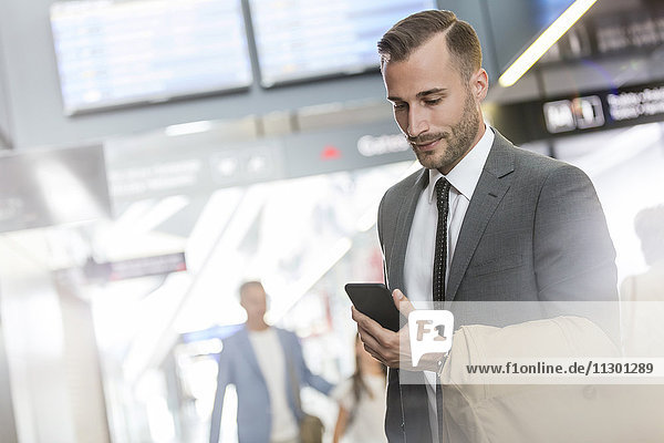 Geschäftsmann SMS mit Handy in der Flughafenhalle