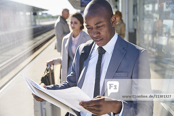 Geschäftsmann liest Papierkram auf dem sonnigen Bahnsteig des Bahnhofs