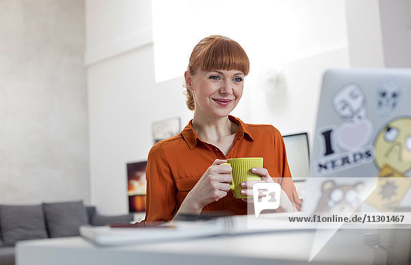 Lächelnde Frau trinkt Kaffee und arbeitet am Laptop