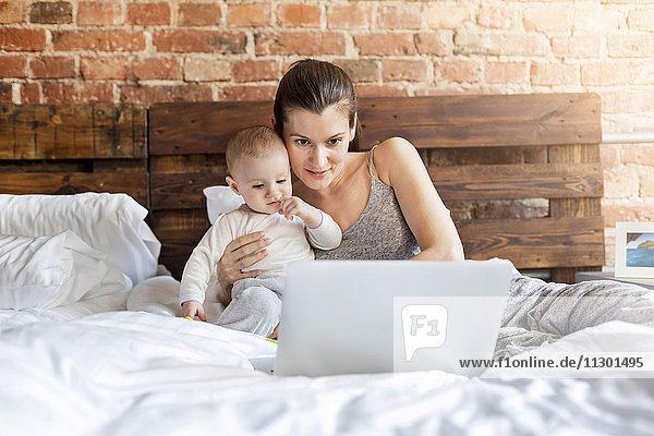 Mother with baby daughter using laptop on bed