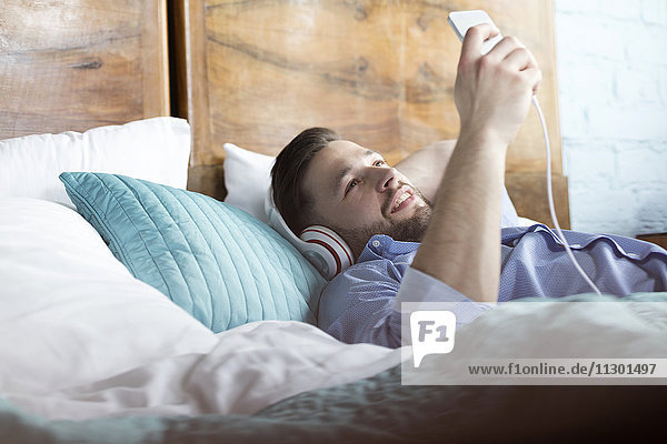 Mann hört Musik mit Kopfhörer und mp3-Player auf dem Bett liegend