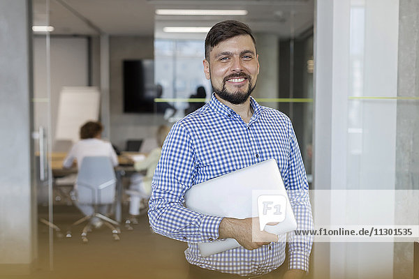 Portrait lächelnder Geschäftsmann mit Laptop im Büro