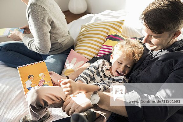 Hochwinkelansicht von Vater und Sohn mit Bilderbuch zum Genießen zu Hause im Bett