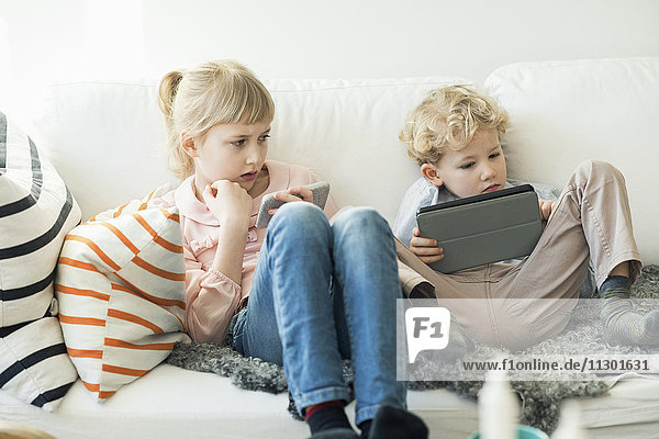 Siblings using digital tablet and mobile phone at home