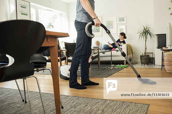 Low section of father cleaning floor with vacuum cleaner at home
