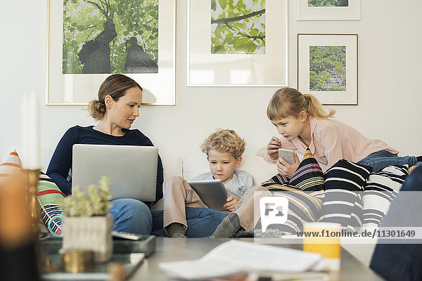 Mutter und Kinder nutzen Technologien auf dem Sofa zu Hause